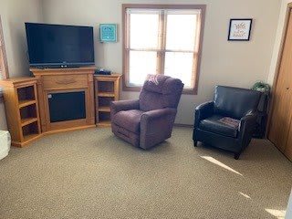 A cozy living room featuring a television, recliner, and armchair with a window letting in natural light.
