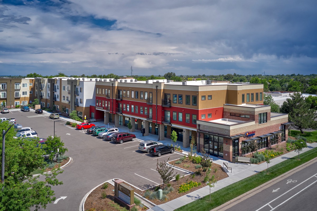 A modern shopping center with a parking lot and a cloudy sky backdrop.