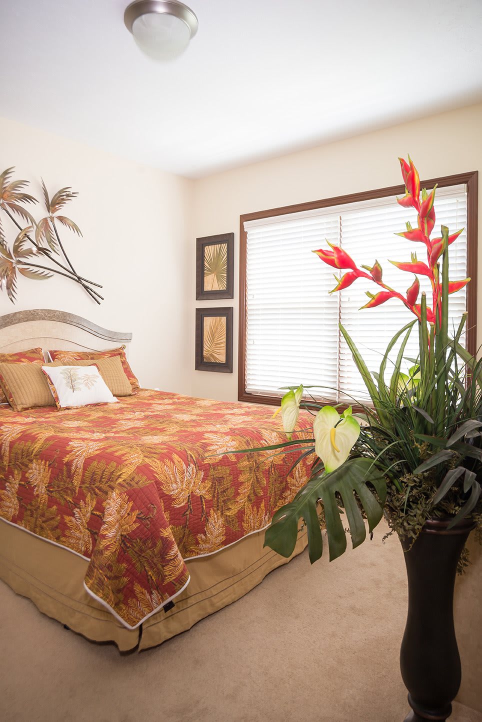 A cozy bedroom with tropical-themed decor, featuring a bed with a patterned bedspread and a potted plant by the window.