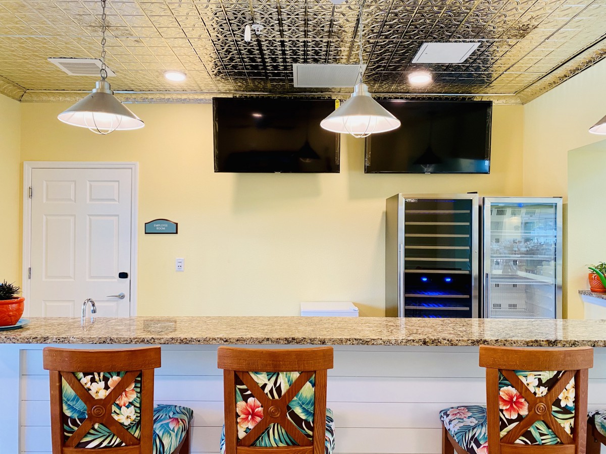 A cozy bar area featuring a granite countertop, floral-patterned chairs, and modern amenities such as televisions and refrigerators.