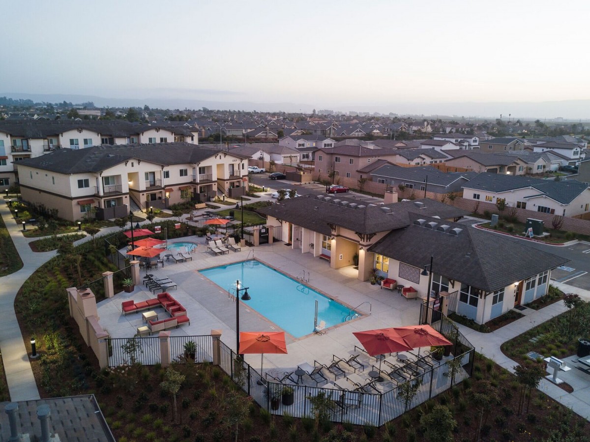 Aerial view of a suburban residential complex with a swimming pool and outdoor seating in the evening.
