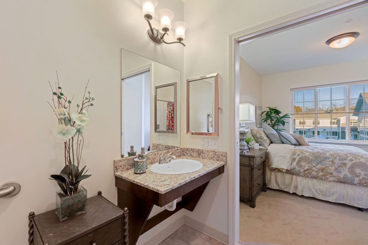 A cozy bathroom with a sink and mirror adjacent to a bedroom.