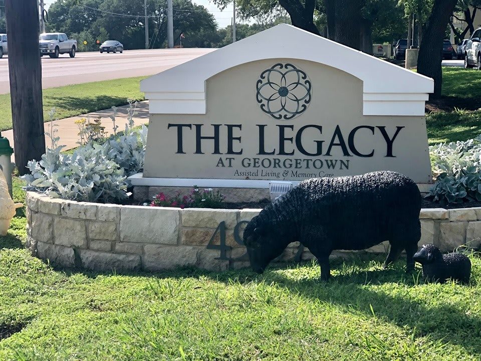 A goat grazes on the grass in front of 'The Legacy at Georgetown' sign.