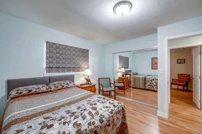 A cozy bedroom with a bed, mirrored closet doors, and a wooden floor.