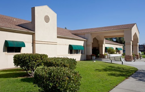 A well-maintained hotel exterior featuring a green canopy and landscaped lawn.