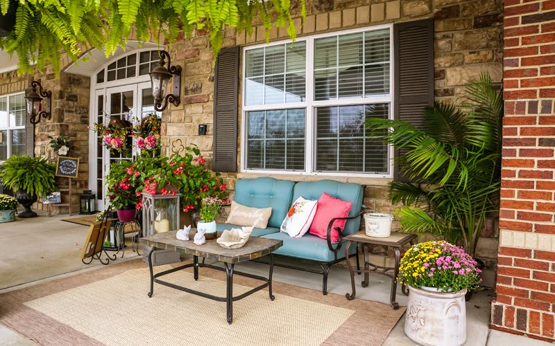 A cozy patio with a cushioned sofa, table, and vibrant plants.