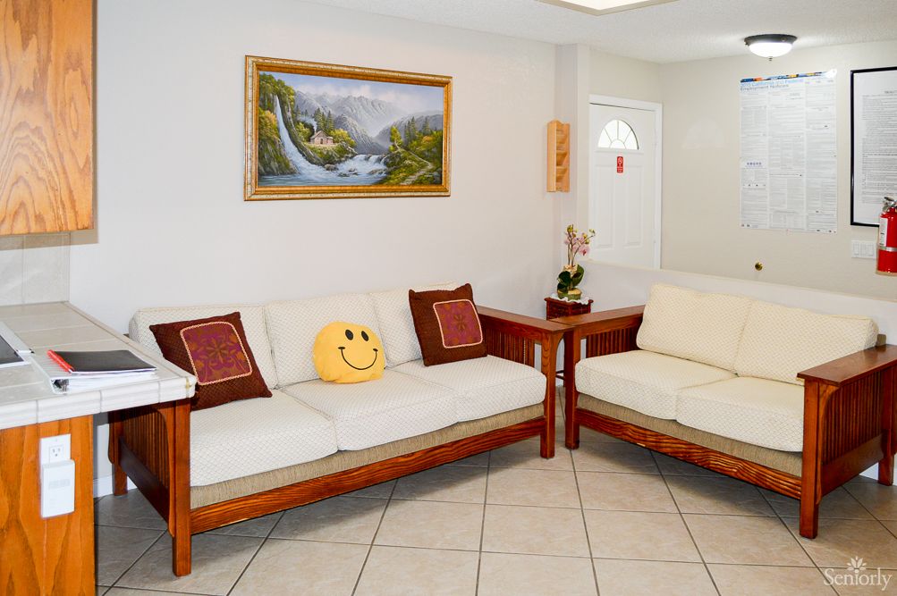 A cozy living room with two wooden sofas, a smiley face pillow, and a landscape painting on the wall.
