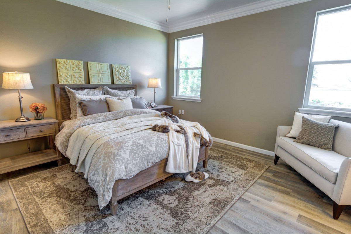 A cozy and elegantly decorated bedroom featuring a neatly made bed, an armchair, a stylish lamp, and a textured rug.