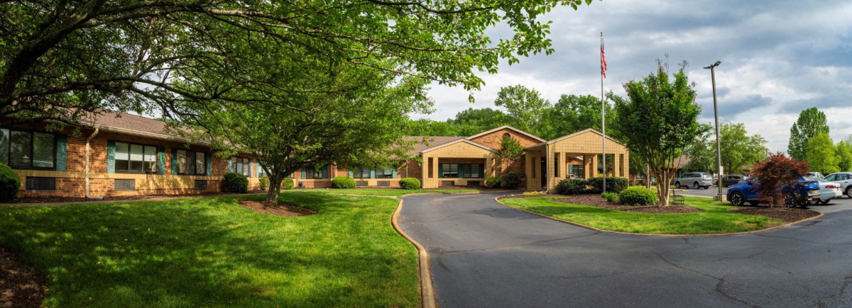 A scenic view of a brick building surrounded by lush greenery and a winding driveway.