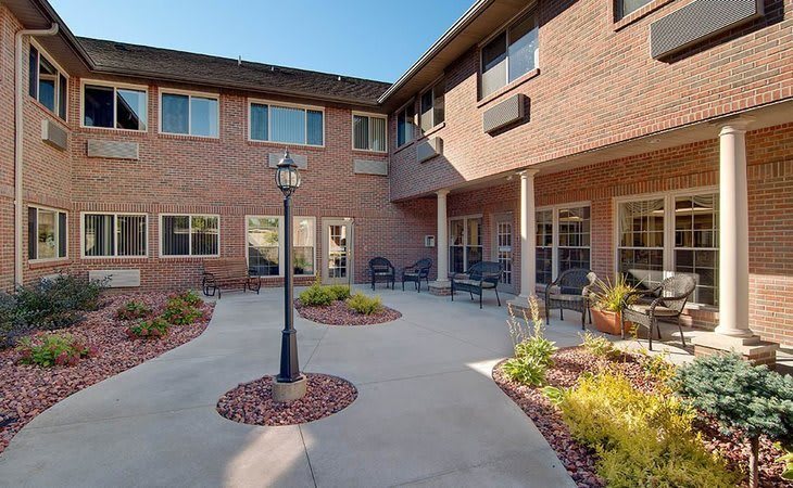 A quiet courtyard with outdoor seating and landscaping surrounded by a brick building.