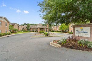 An apartment complex with a landscaped parking area and surrounding trees.
