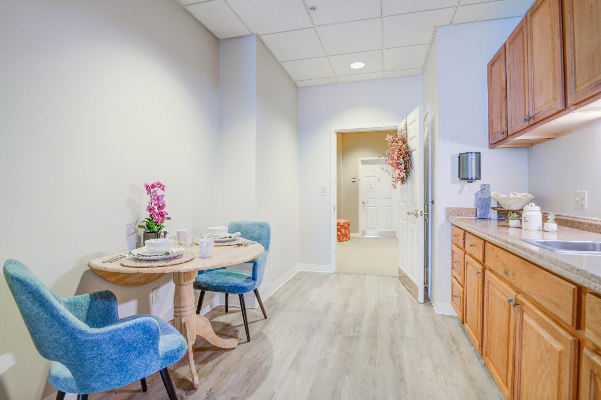 A modern kitchen with a small dining area featuring blue chairs and a wooden table set with flowers.