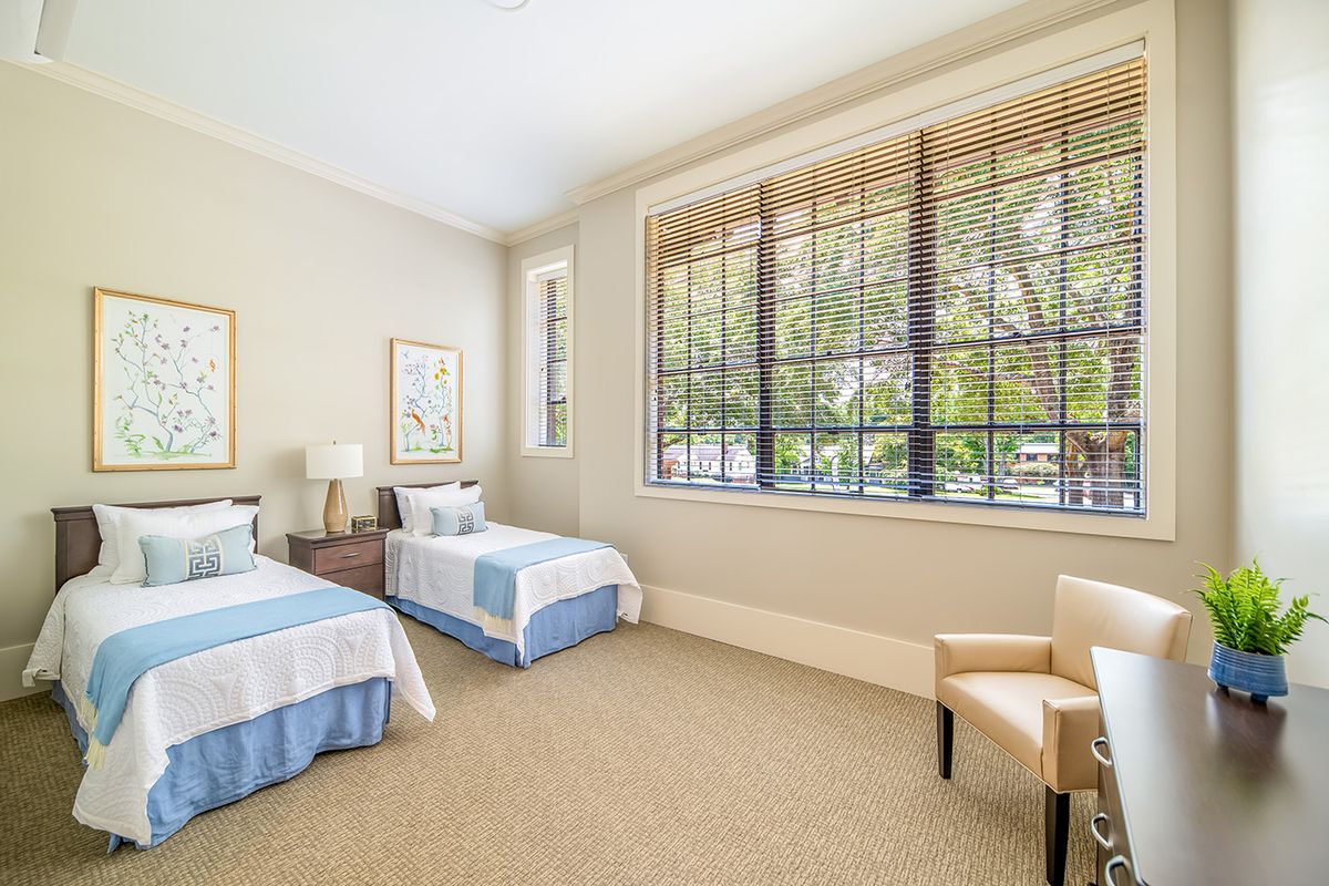 A bright bedroom featuring twin beds, large windows, and neutral-colored decor.