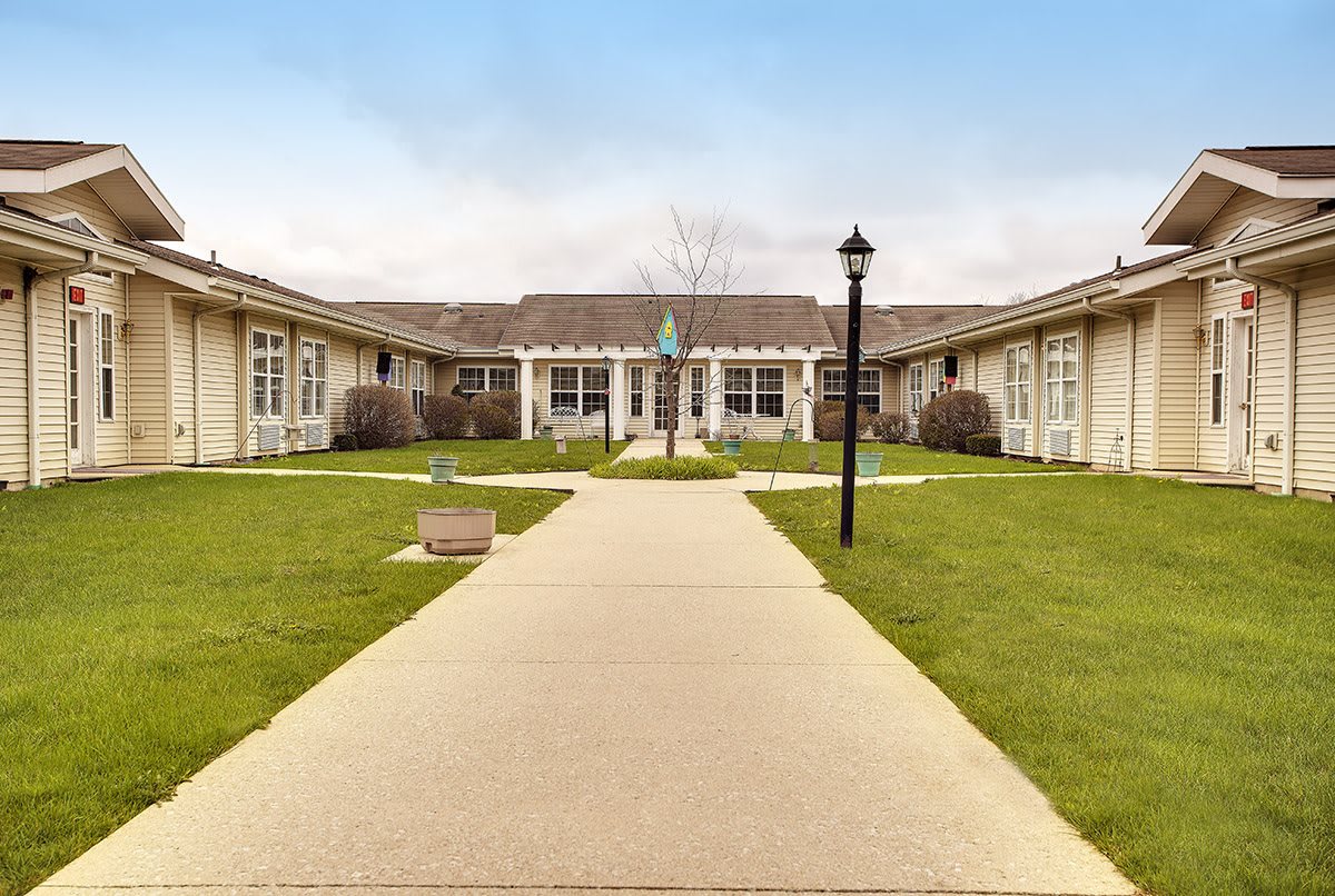 A serene courtyard featuring a well-maintained lawn and a central pathway leading to the building entrance, illuminated by a lamppost.