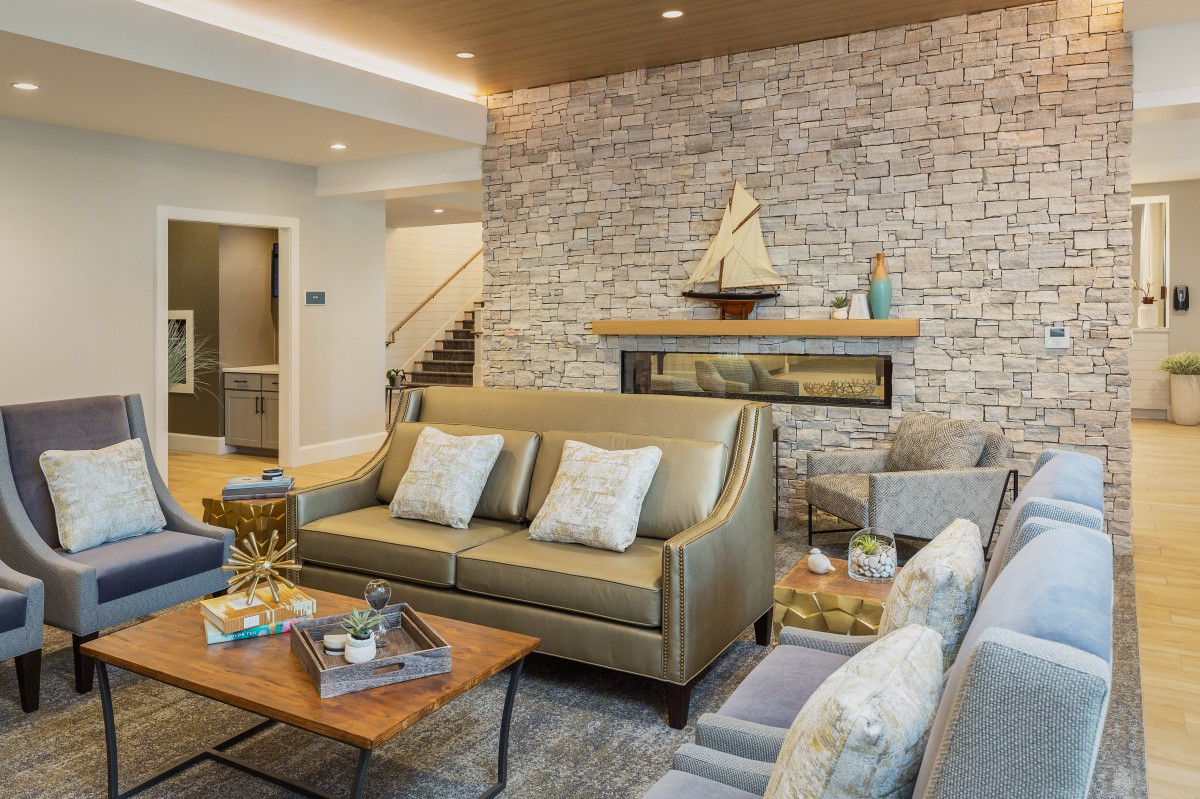 A modern living room with a stone fireplace, stylish furniture, and a wooden model sailboat on the mantel.