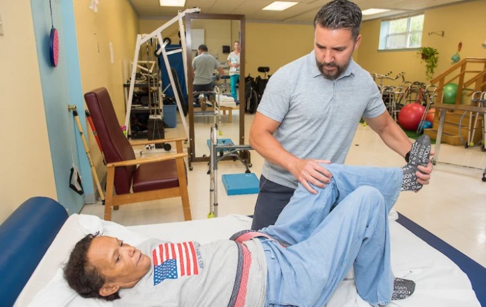 A therapist assists a patient with leg exercises during a physical therapy session.