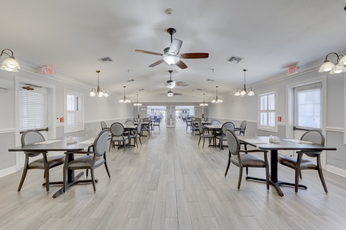 A spacious dining room with neatly arranged tables and chairs, featuring ceiling fans and elegant lighting.