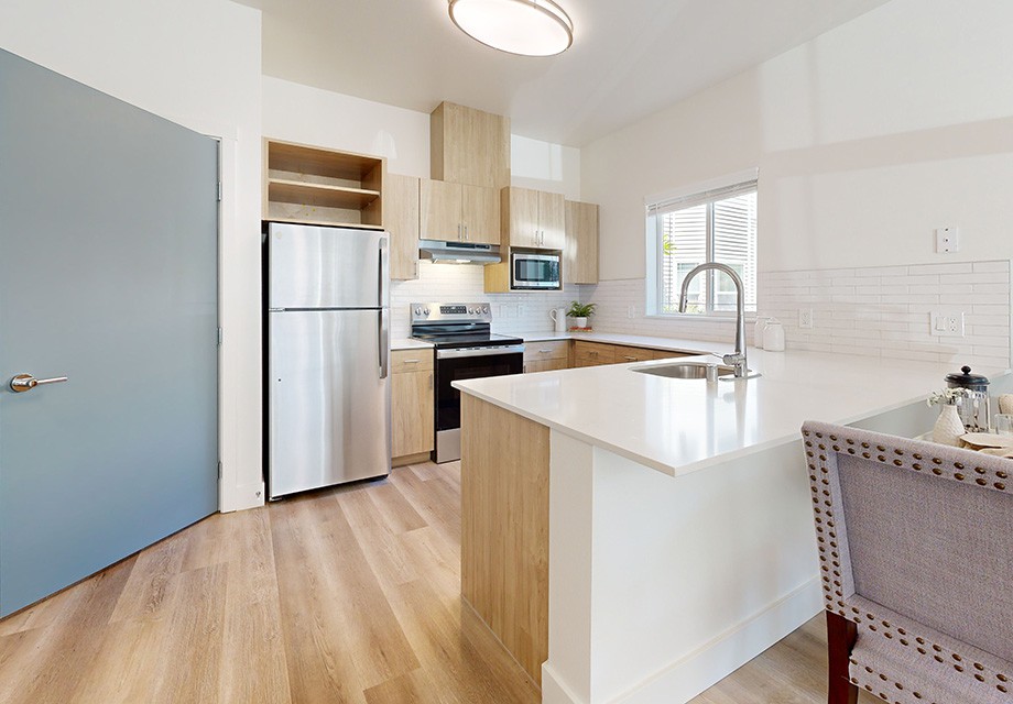 A modern kitchen with wooden flooring, featuring stainless steel appliances and a spacious countertop.