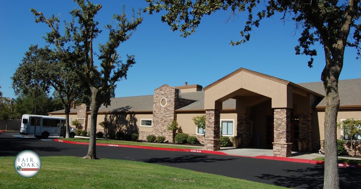 A single-story suburban building with a prominent entrance and surrounding trees under a clear blue sky.