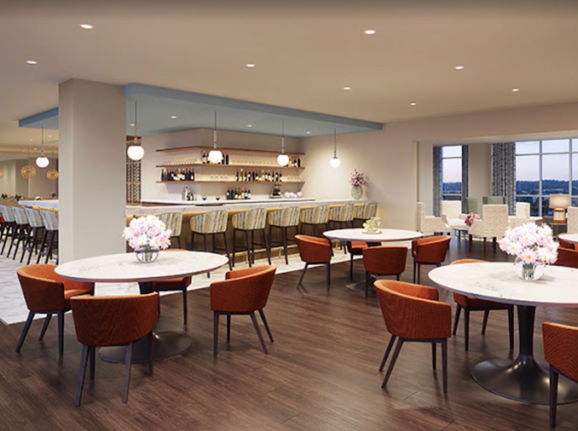 A modern restaurant interior featuring round tables, comfortable seating, and a stylish bar area.