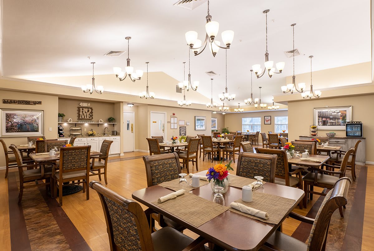 A well-lit dining room with neatly arranged tables and chairs, adorned with elegant chandeliers and a wooden floor.