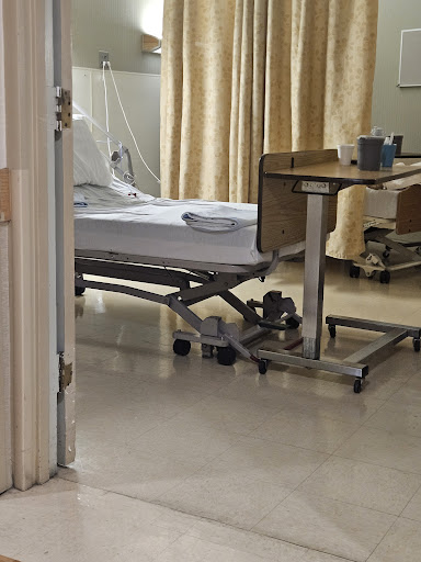 A view of a patient room in a hospital, featuring an unoccupied hospital bed and medical equipment.