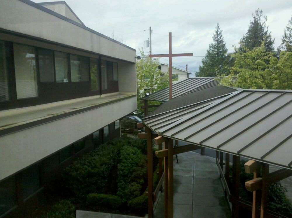 A view of a modern building with a cross, surrounded by trees under an overcast sky.