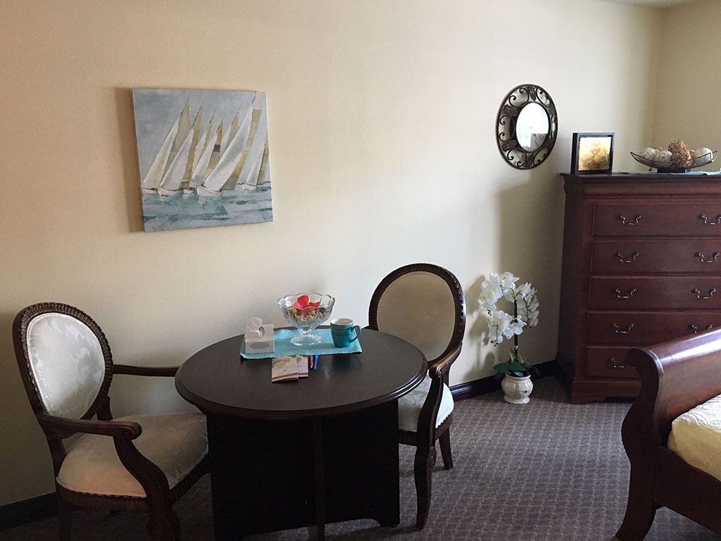 A cozy interior featuring a round dining table with chairs, adorned by a sailing-themed painting and decorative elements including a mirror and potted plant.