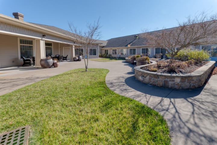 A sunny courtyard surrounded by buildings with a paved walkway and green lawn.