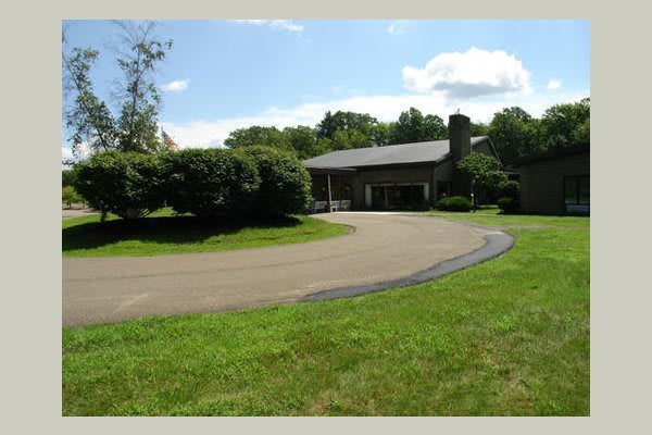 A suburban house with a circular driveway surrounded by lush greenery.