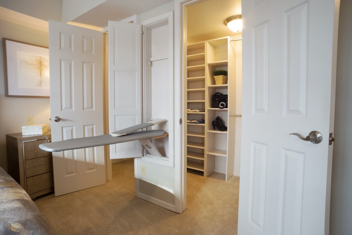 A walk-in closet with built-in shelving and a fold-out ironing board.