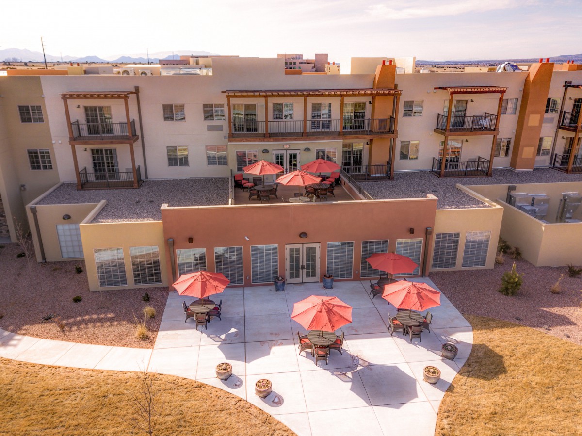 A modern apartment complex with outdoor seating areas and red umbrellas, showcasing its spacious balconies and patio.