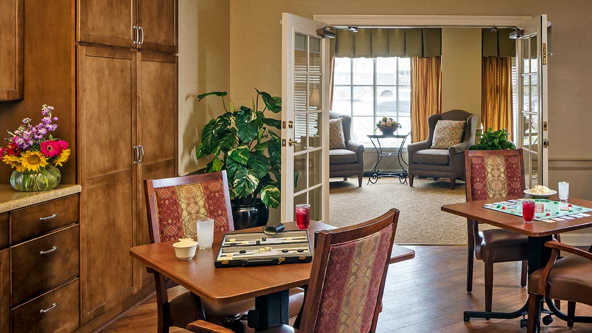 A cozy living room with a table and chairs, featuring a large plant and a window view.