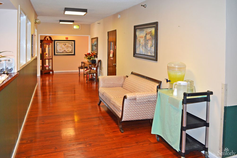 A well-lit hallway with wooden floors, a sofa, artwork on the walls, and a drinks station.