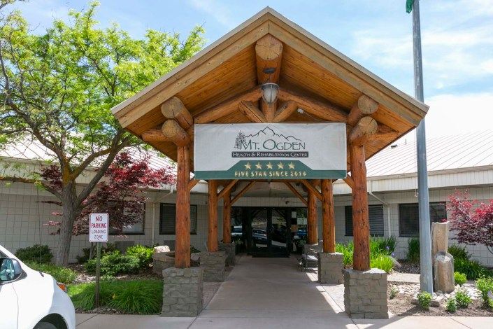 Entrance of a building with a wooden canopy and landscaped surroundings.