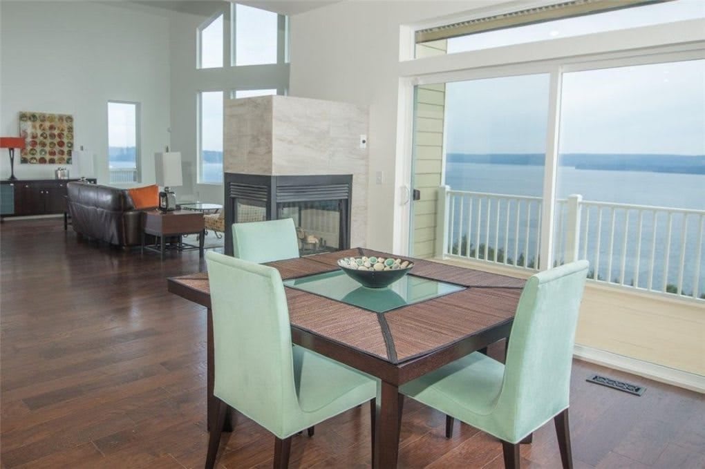 A modern dining room with a table and chairs, featuring large windows offering an ocean view.