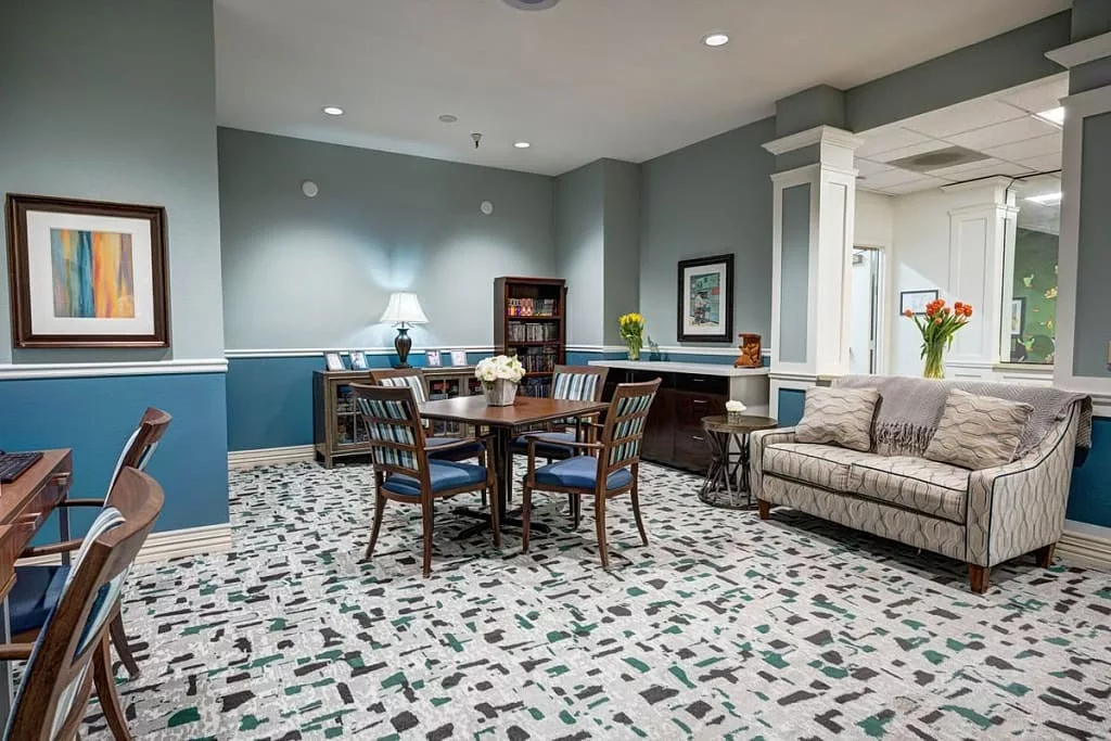 A cozy living and dining area featuring a round wooden table surrounded by chairs, a comfortable sofa, and a bookshelf in the corner.