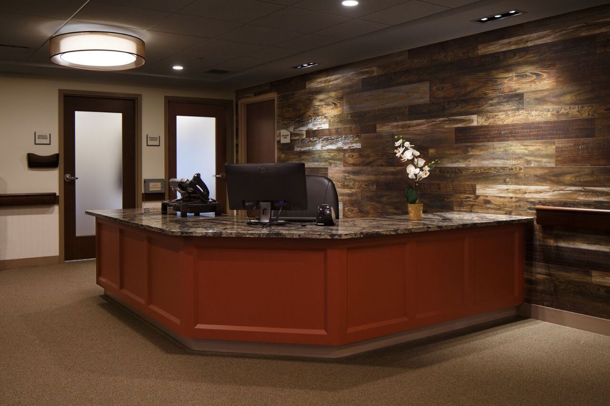 A modern office reception area with a wooden desk and wall paneling.