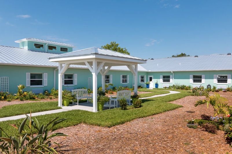 A peaceful courtyard with a central gazebo surrounded by a well-maintained garden and light blue buildings.