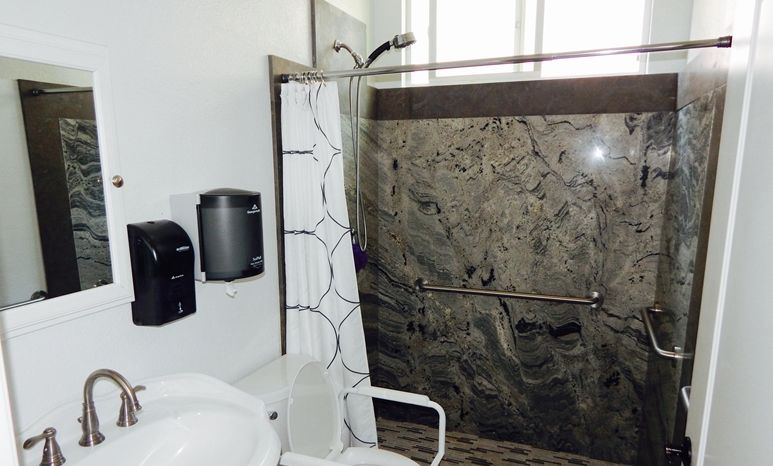An accessible bathroom featuring a shower with a grab bar, toilet, and curtain.