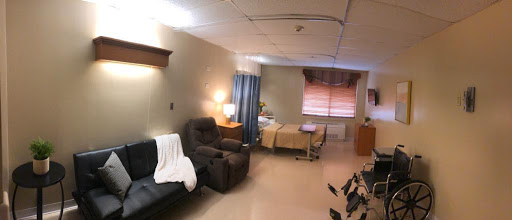 A spacious and well-lit hospital patient room featuring a bed, comfortable seating area, and curtains for privacy.