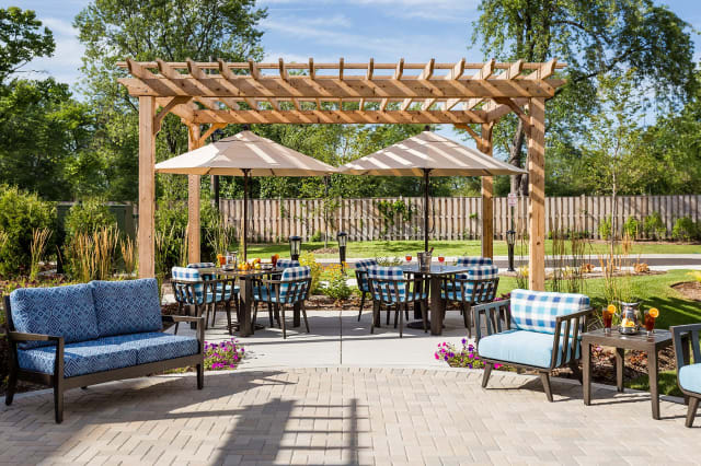 A cozy outdoor patio area featuring a wooden pergola, comfortable seating with cushions, and large umbrellas on a sunny day.