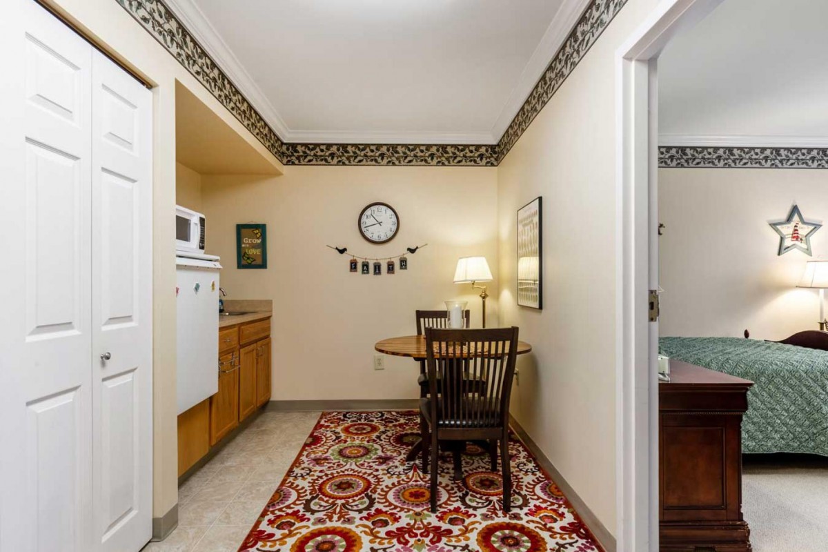 A cozy dining area with a table set for two, featuring a decorative rug and wall clock.