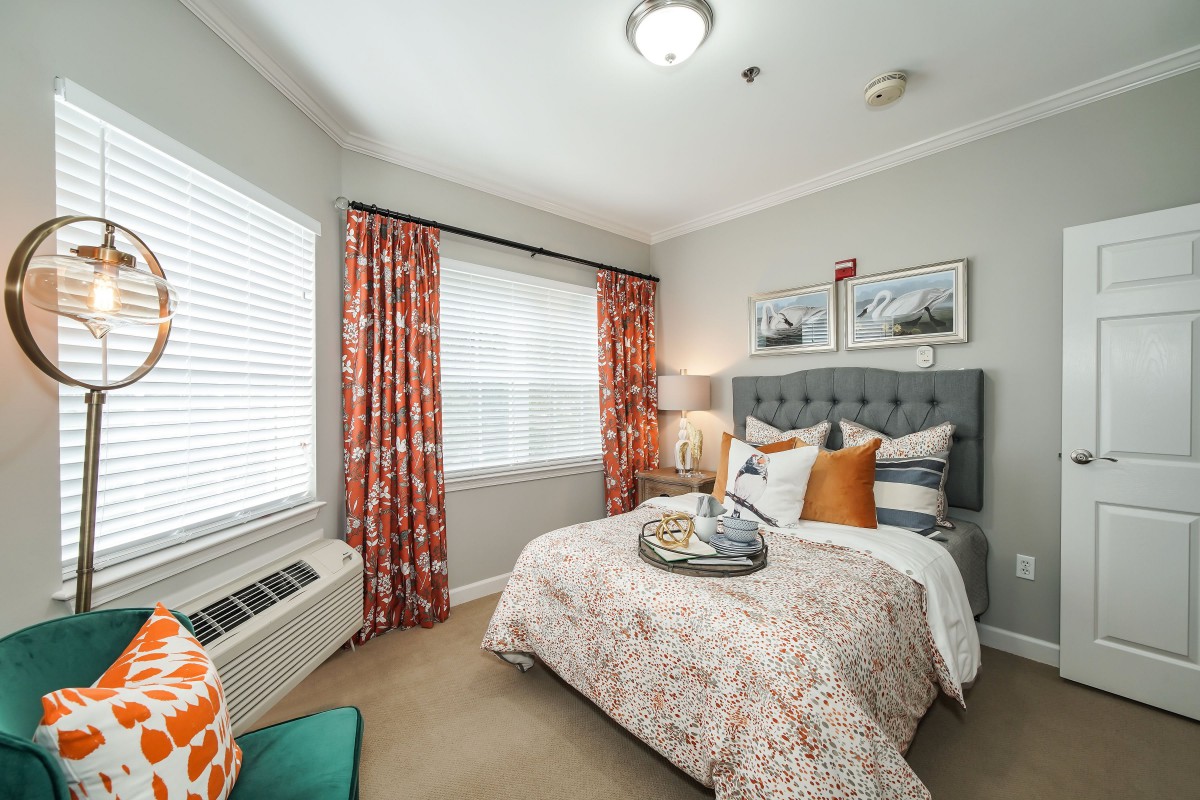 A cozy bedroom with a neatly made bed, vibrant curtains, and decorative pillows.