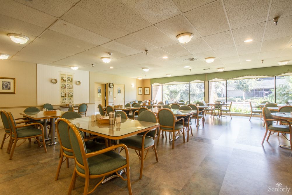 An empty dining area with neatly arranged tables and chairs, featuring large windows for natural light.
