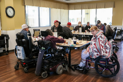 A group of individuals in wheelchairs enjoying a meal together in a dining area.