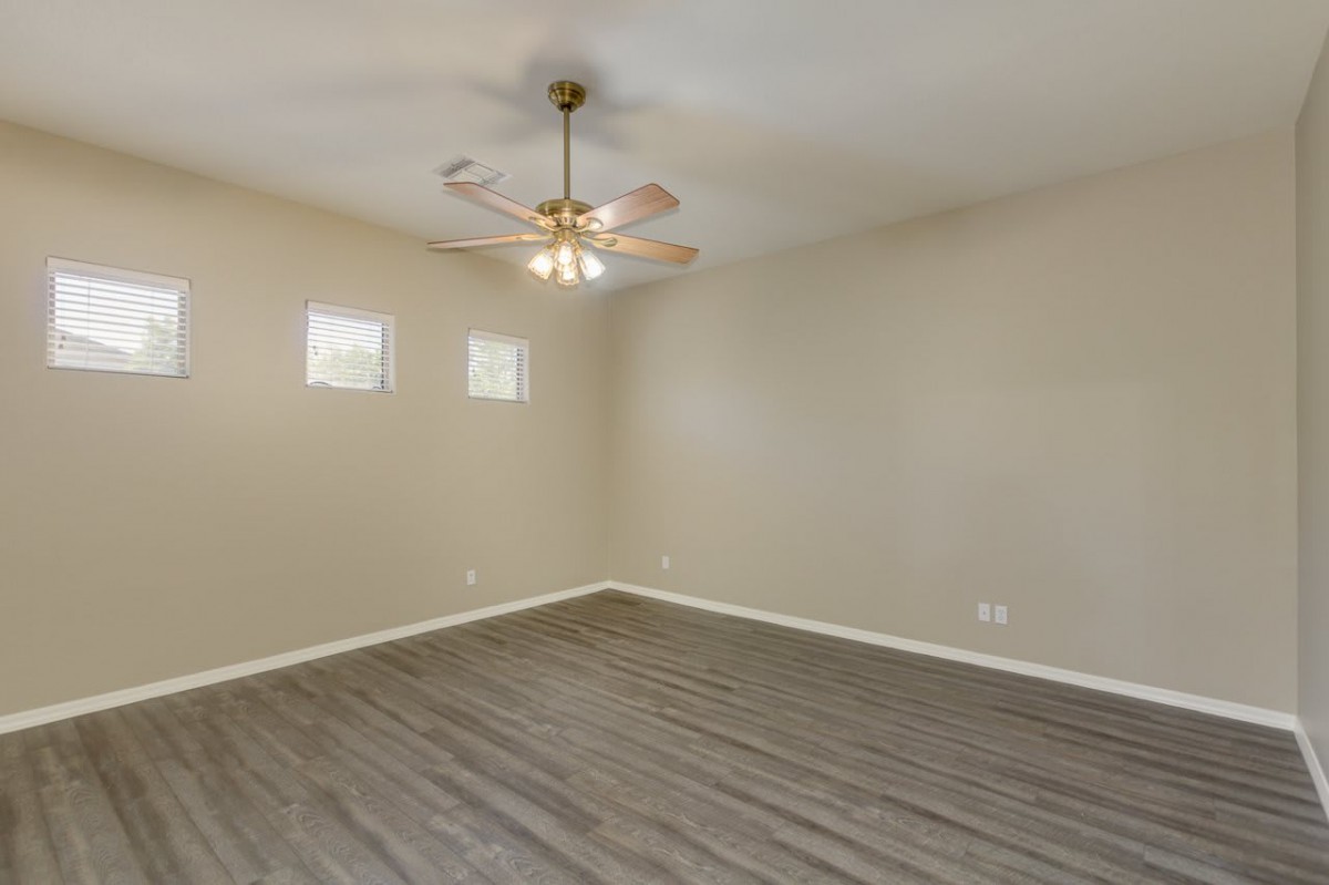 An empty room with a ceiling fan, laminate flooring, and two small windows.