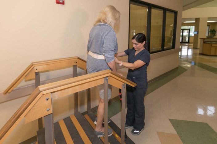 A healthcare professional assists a patient with stair exercises during physical therapy.