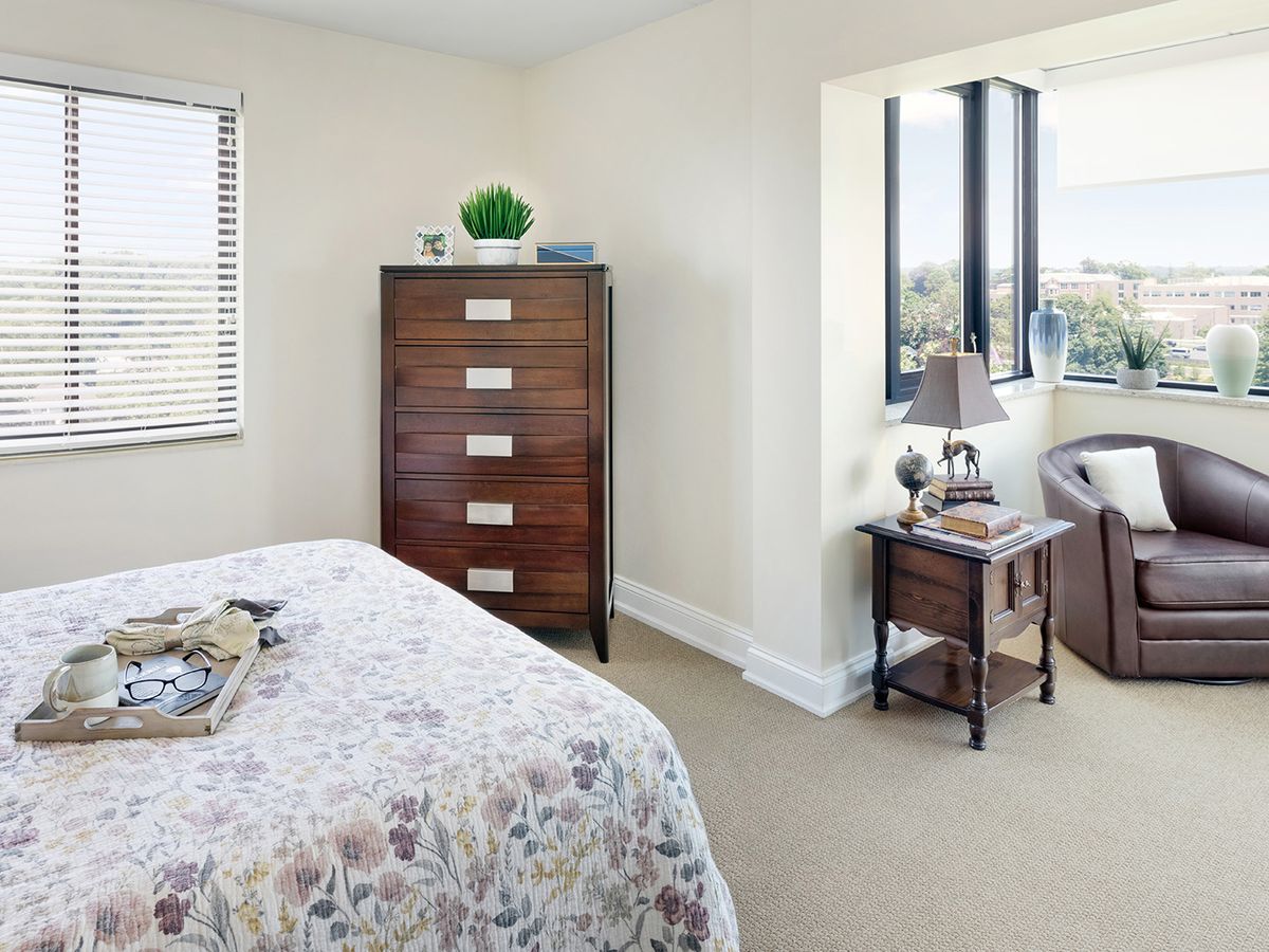 A cozy bedroom with a chest of drawers, bed, and a comfortable seating area by the window.