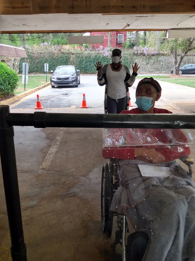 A person in a wheelchair is being assisted outside, while another individual stands behind them with their hands raised.